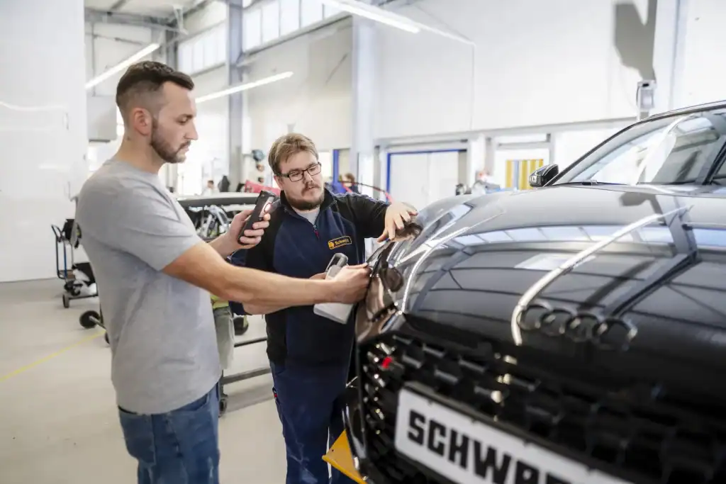 Werkstattmitarbeiter bei der Bestimmung des richtigen Farbtons für die fachgerechte Lackierung nach einem Unfallschaden.
